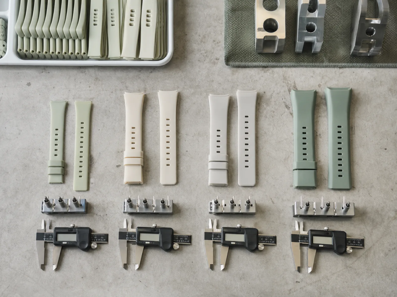 Anonymized solid-color custom silicone watch bands laid out by lug width on a QC bench with pin-gauge fixtures at a custom silicone watch band manufacturer