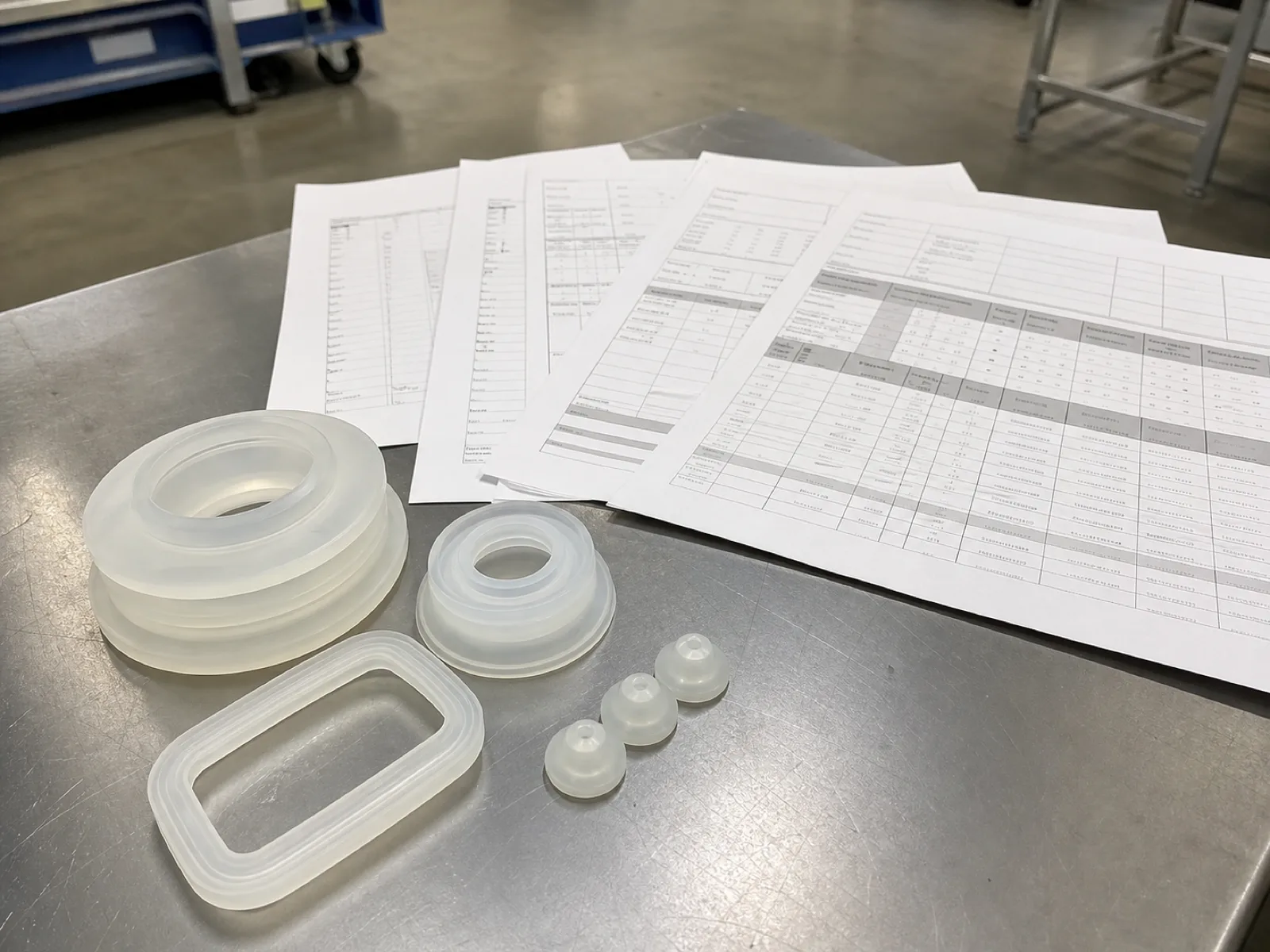 Certificate of analysis and extractables test report on a QC bench beside cured LSR and HCR silicone samples, documenting cure system, hardness, and food-contact compliance per batch