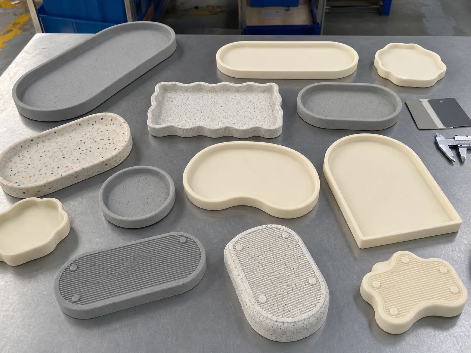 Flat-lay of concrete-look, terrazzo-look, and warm-cream matte silicone decorative trays arranged on the Wetop QC bench in Dongguan under D65 daylight-simulation lighting, catchall and vanity tray shapes at Shore A 55 with anti-slip base