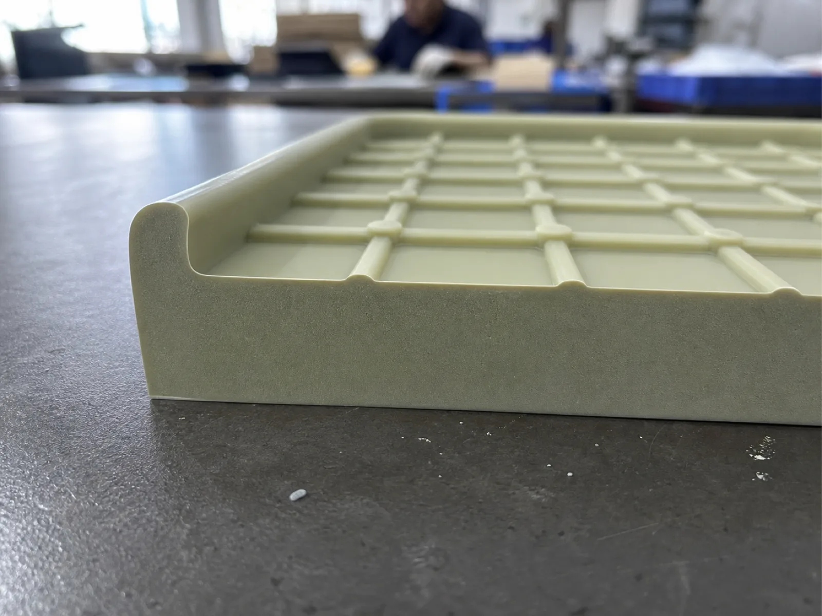 Cross-section detail of a custom silicone drip mat at Wetop's Dongguan QC bench showing 8 mm base thickness, 4 mm raised perimeter lip, and 3 mm cross-hatched drainage channels on the top surface, sage-and-cream platinum-cured PDMS at Shore A 65