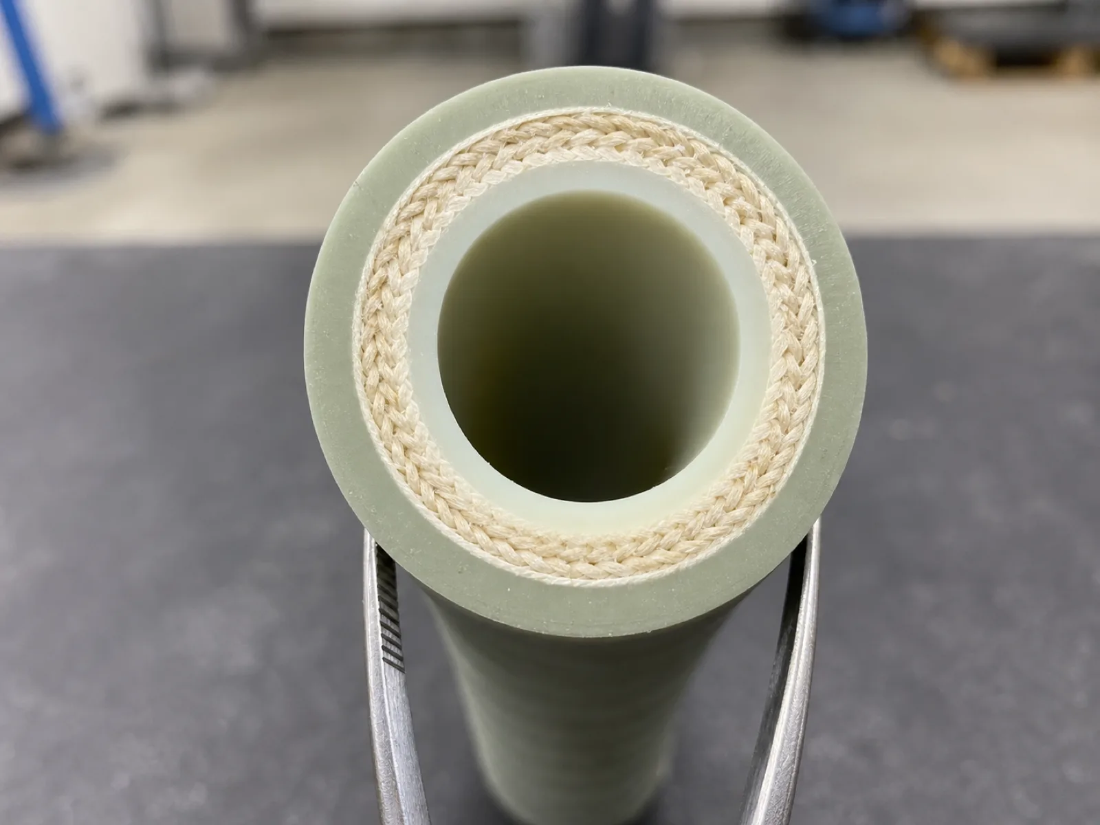 Razor-cut cross-section of a multi-ply reinforced silicone hose on a matte QC bench, showing the inner silicone liner, an aramid textile braid ply, and the outer silicone cover under magnification