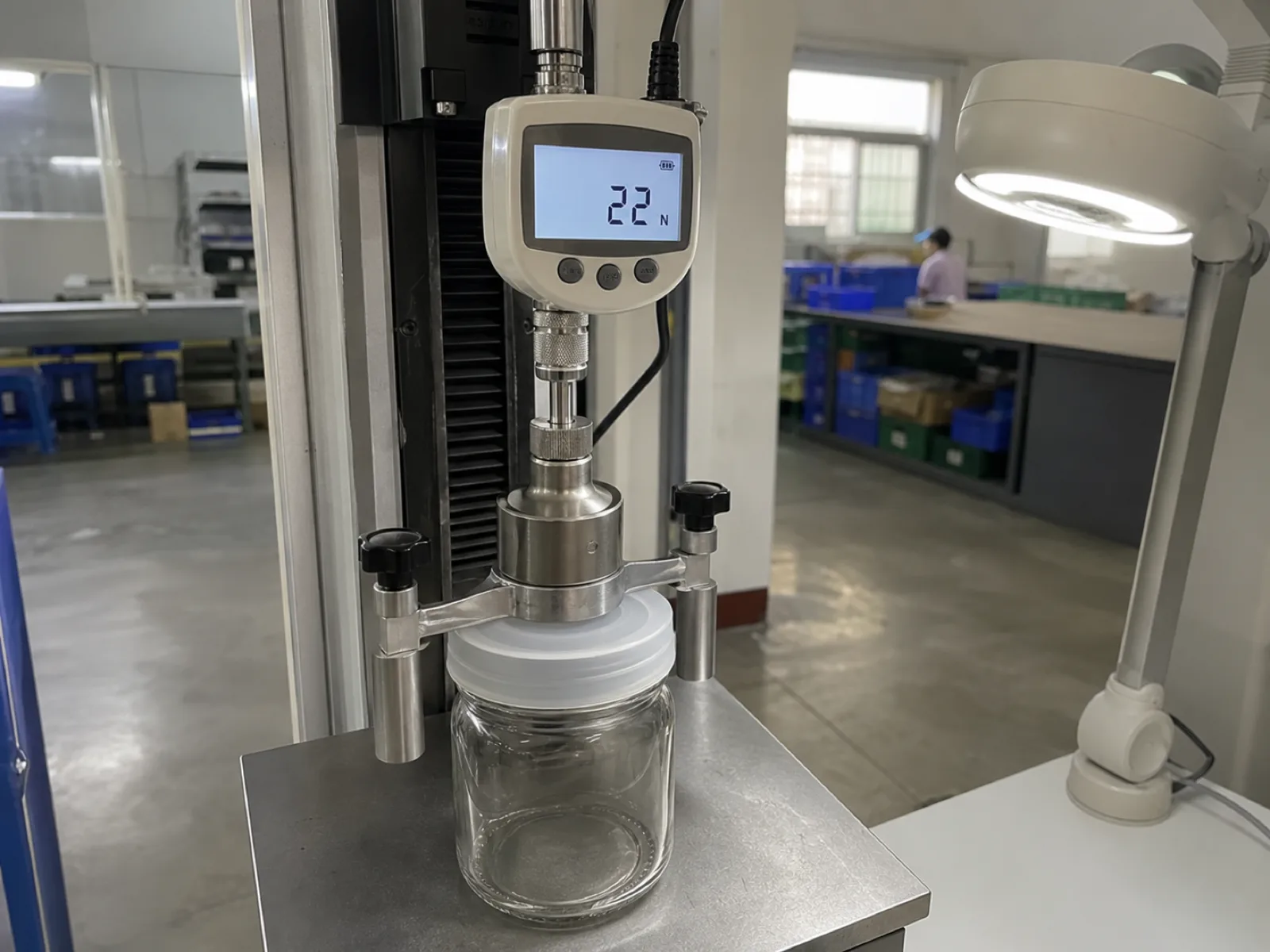 Wetop QC bench pull-off force test rig with a calibrated digital gauge measuring the vacuum pull force on a platinum-cured silicone regular-mouth Mason jar lid sealed onto a generic clear glass jar reading 22 newtons under D65 inspection light in Dongguan