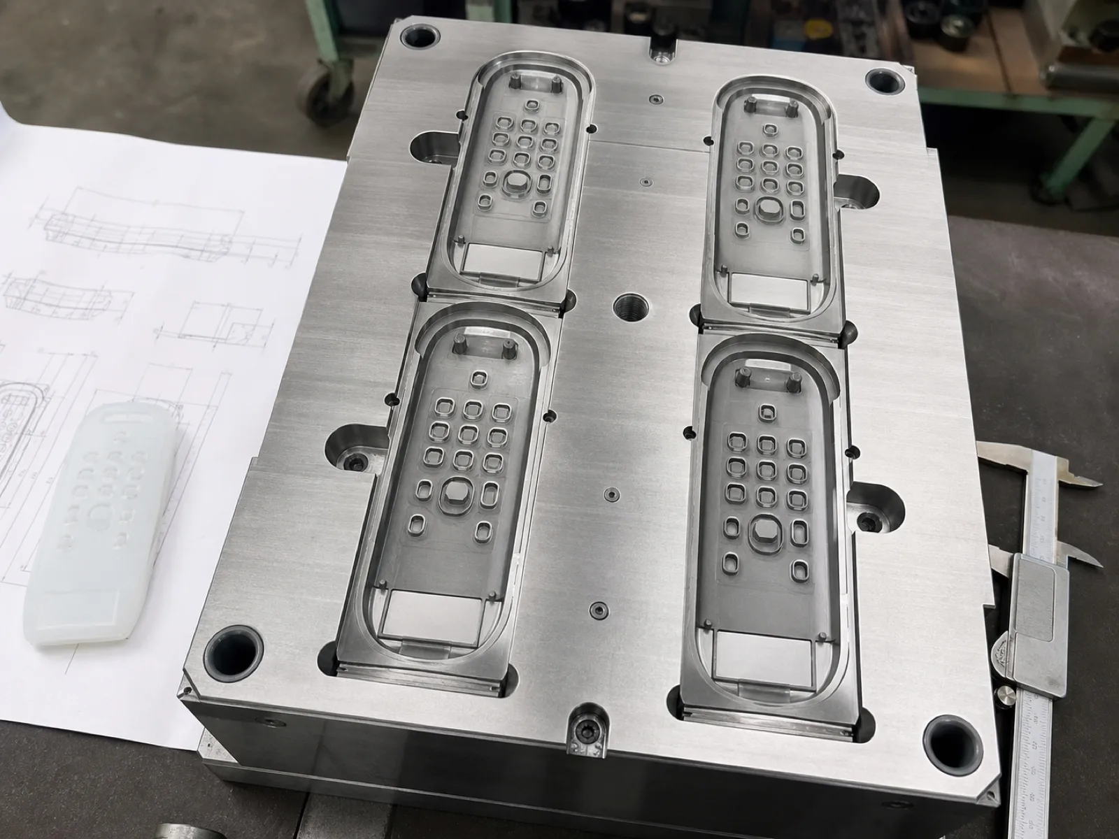 Compression-mold cavity for a custom silicone remote control cover showing button-well cores, IR-window window inset, and battery-door lip geometry on a Wetop tool bench
