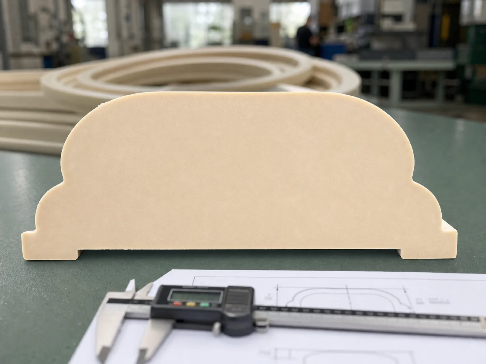 Cross-section view of a compression-molded silicone rubber gasket cut on the bandsaw, matte-satin platinum-cured VMQ silicone showing uniform bulk density with no voids, void-free profile geometry on sage QC bench next to a caliper and a printed drawing, natural workshop light